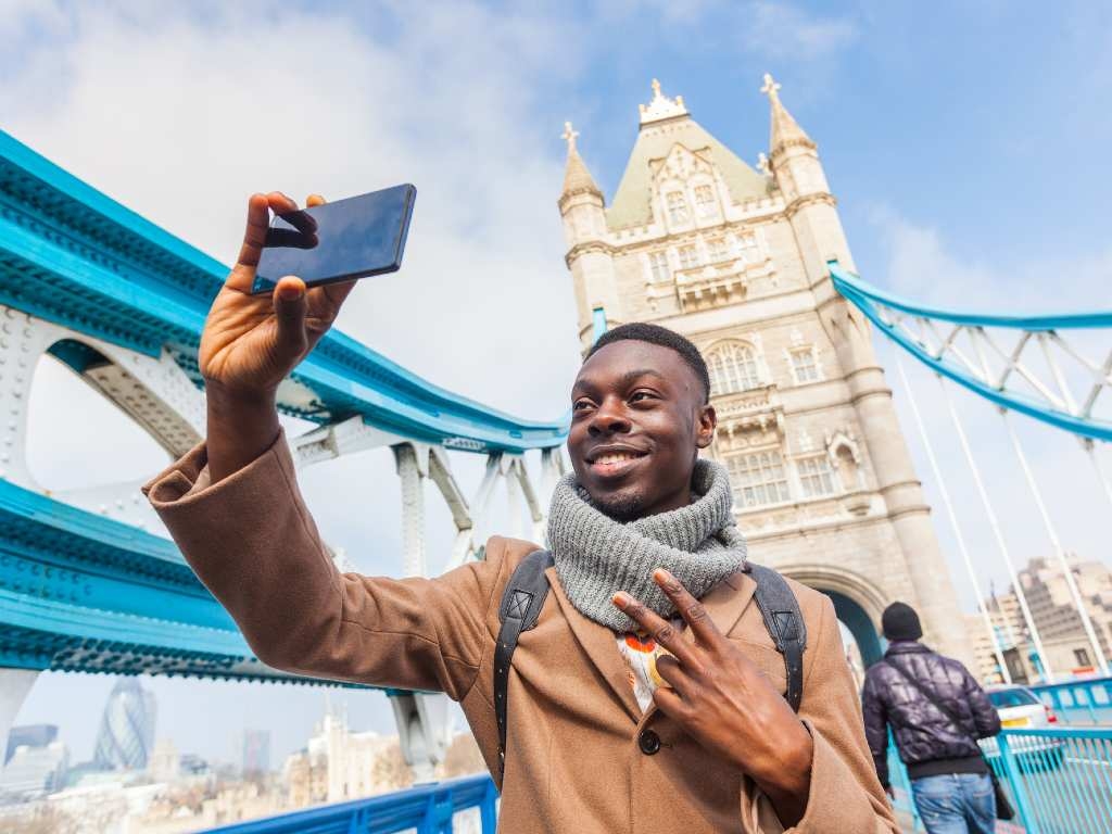 smiling man taking selfie in front of London Bridge.