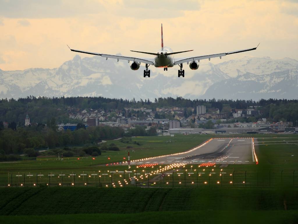 Plane landing on runway with mountains in the background.